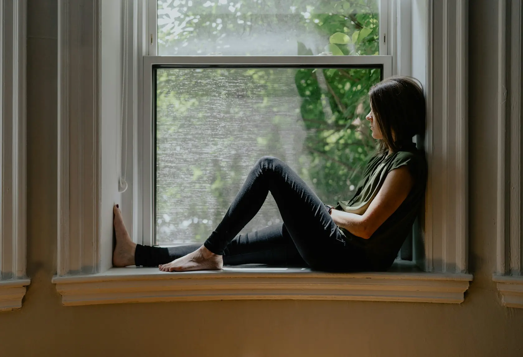 Femme assise sur le rebord d’une fenêtre, pensive