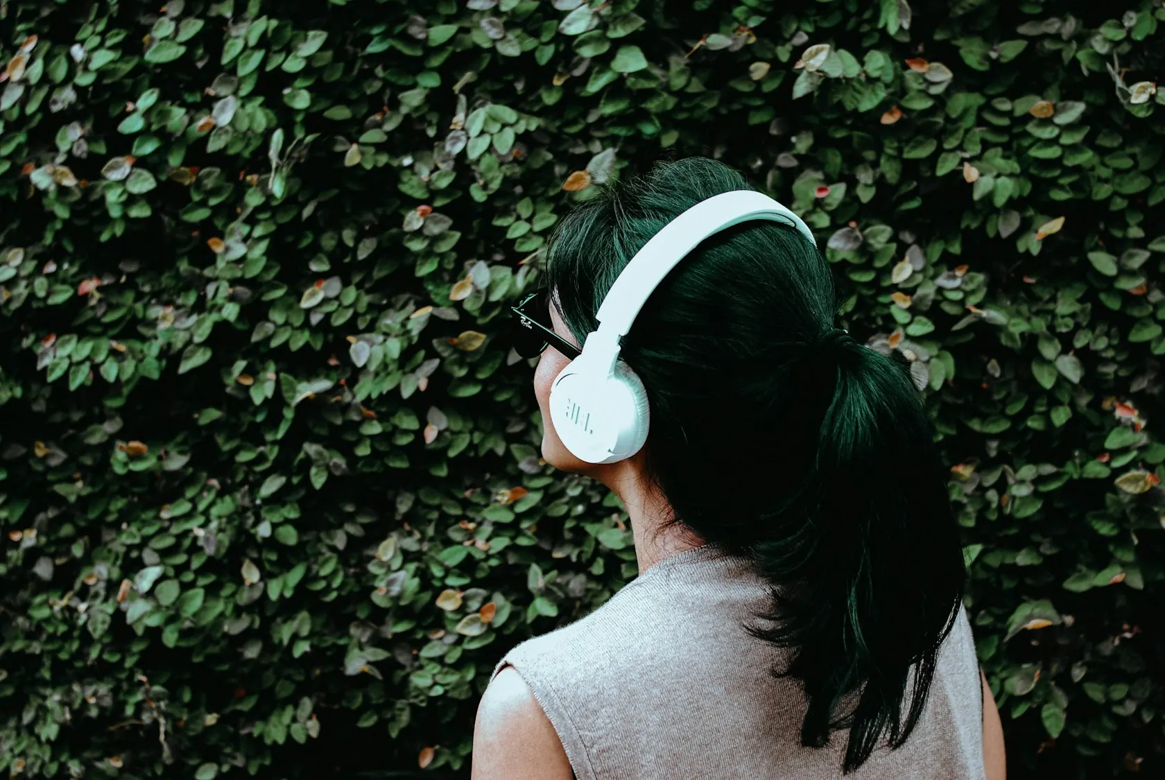 Femme de dos écoutant avec un casque blanc devant un mur végétal